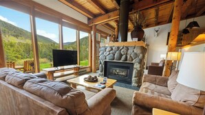 A cozy living room with a stone fireplace, leather sofas, a television, and a scenic mountain view through large windows. - Evergreen Condominiums by Vail Resorts (Keystone)