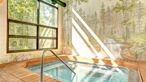 A hot tub with a view of a forest through a window, a wooden deck, and a tiled wall with a forest mural. - Evergreen Condominiums by Vail Resorts (Keystone)