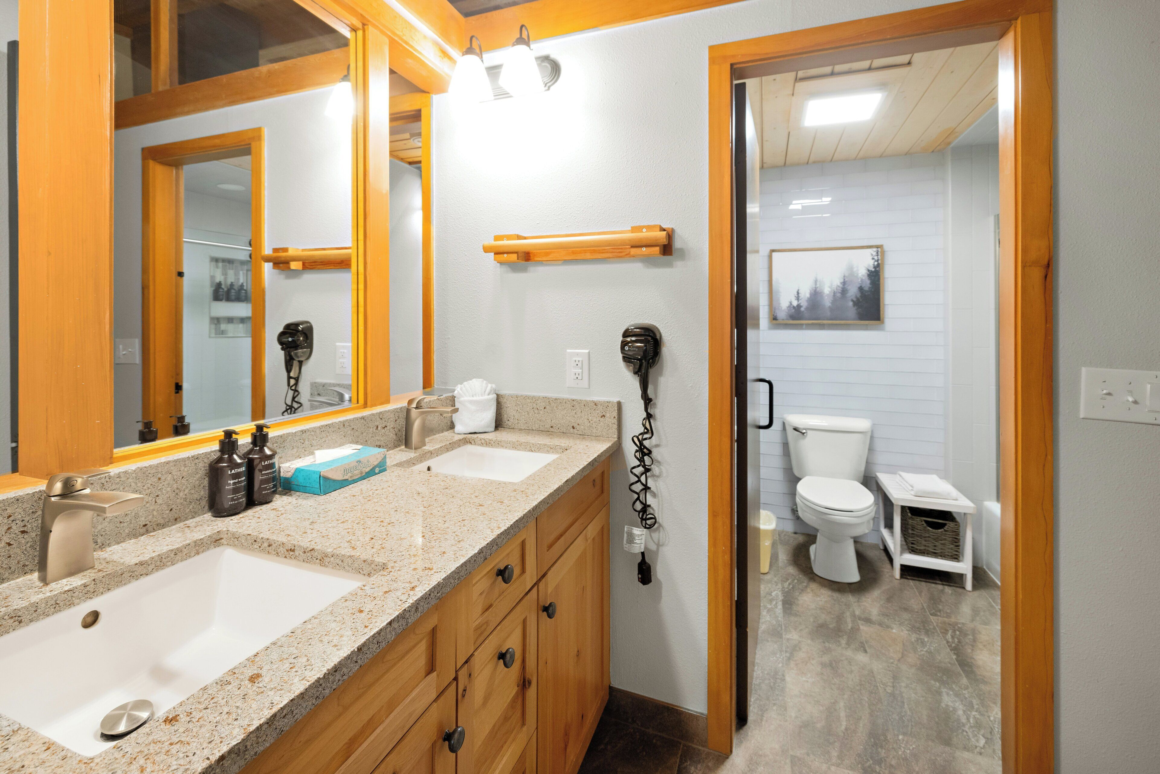 Une salle de bain avec un double lavabo, des meubles en bois, un miroir, un porte-serviettes et des toilettes.