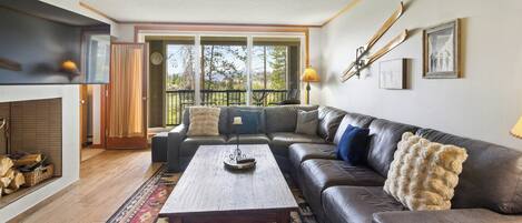 A living room with a fireplace, a large sectional sofa, a coffee table, and a view through a glass door.
