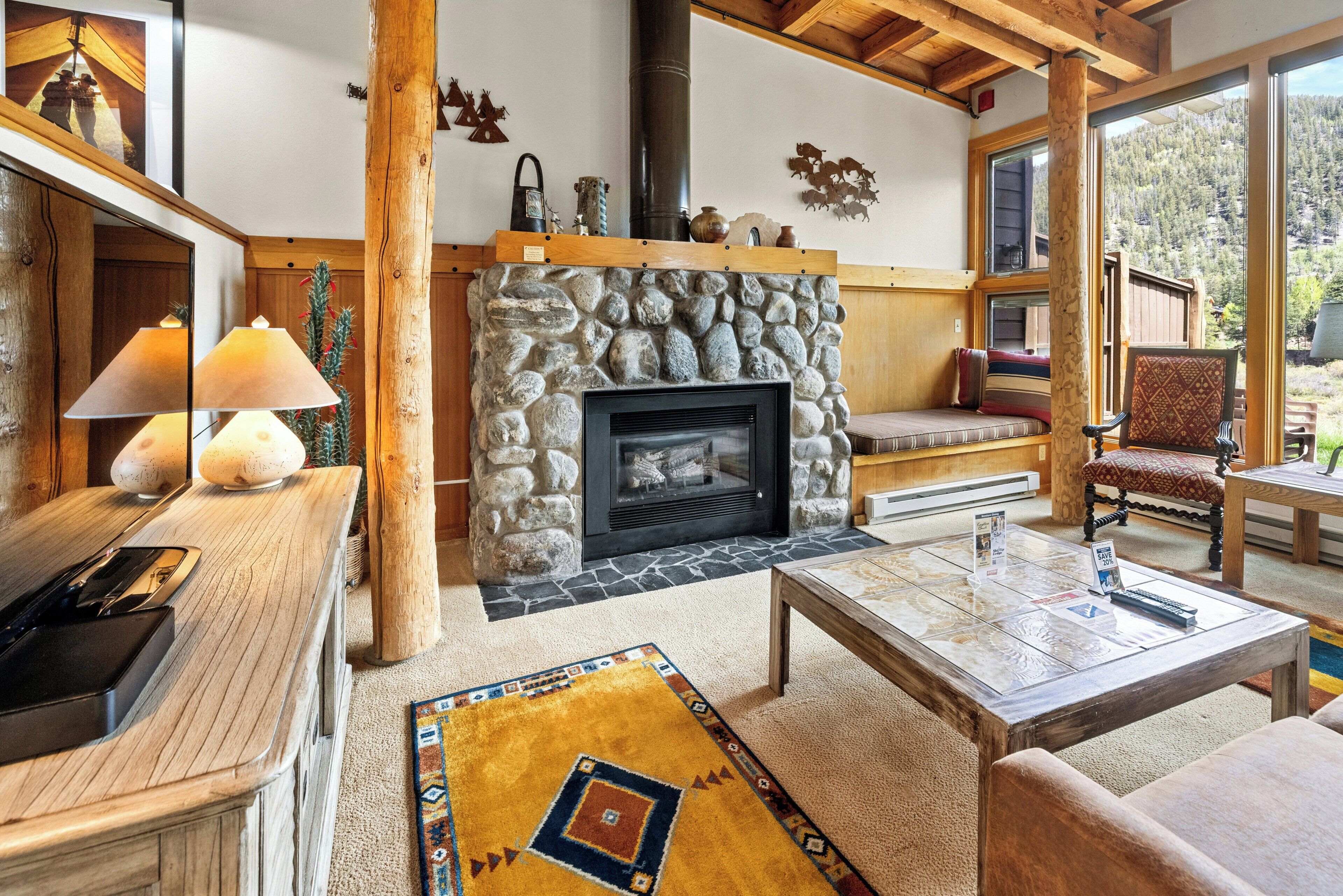 Un interior acogedor con chimenea de piedra, mobiliario de madera y vistas al exterior.