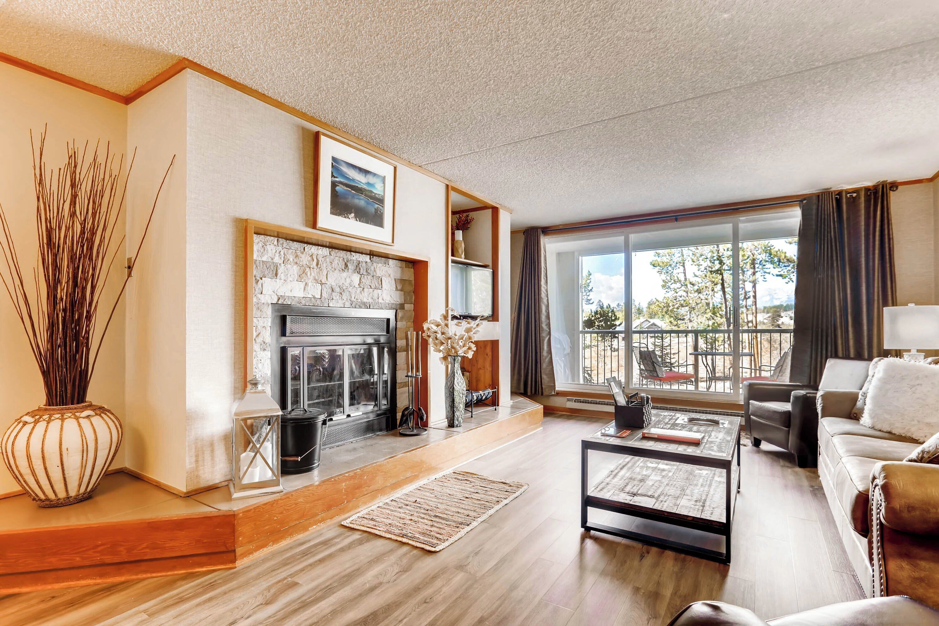 A modern living room with a fireplace, a sofa, a coffee table, and a view of the outdoors.