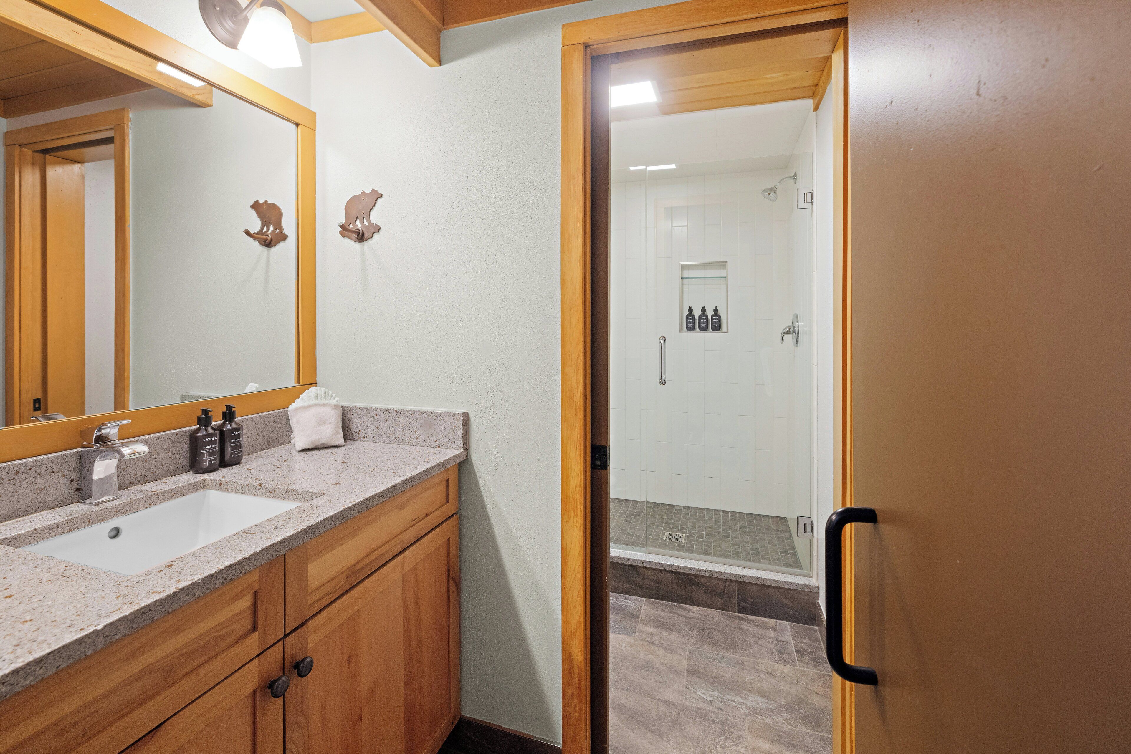 A bathroom with a sink, mirror, wooden cabinets, and a shower area.