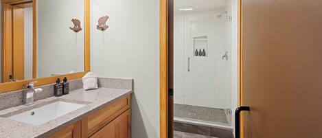 Une salle de bain équipée d’un lavabo, d’un miroir, de meubles en bois et d’un espace douche.