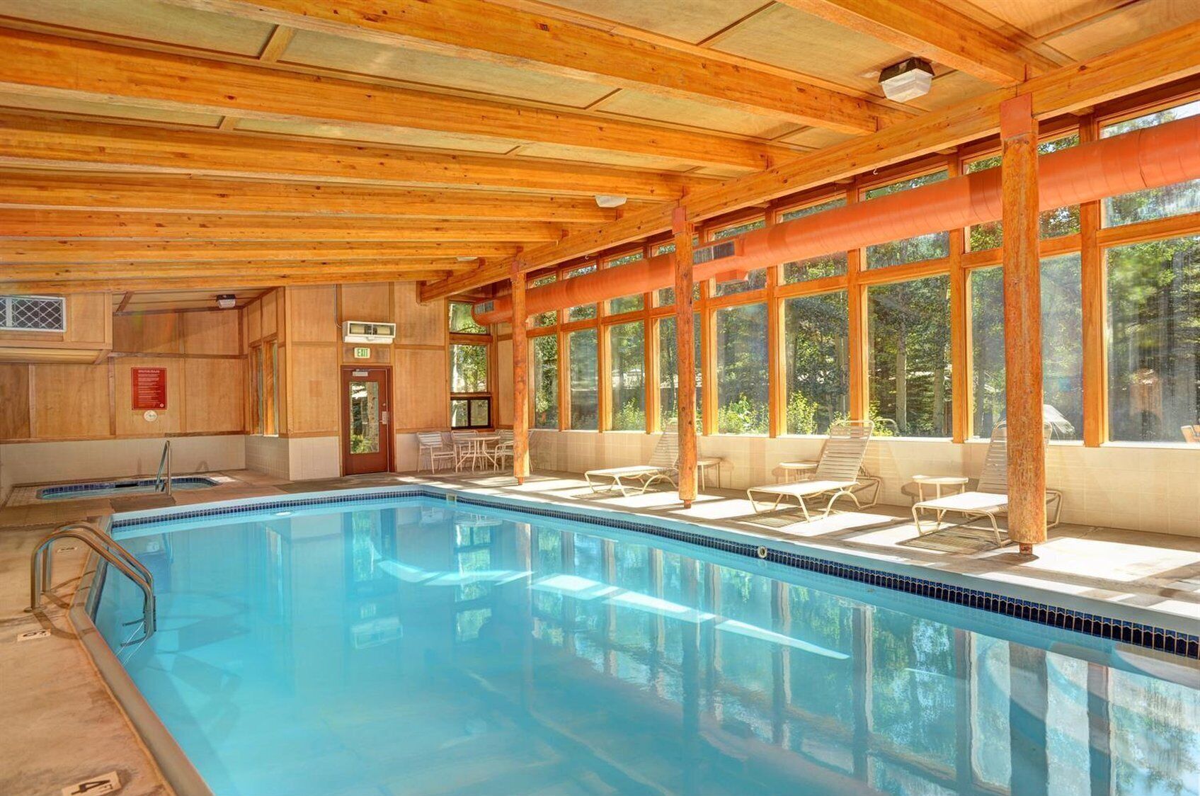 A pool area with a wooden ceiling, large windows, and lounge chairs.