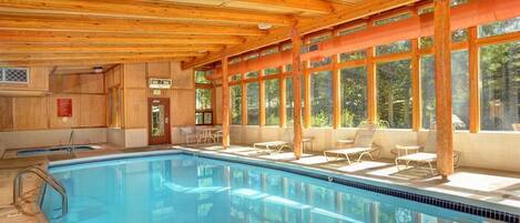 A pool area with a wooden ceiling, large windows, and lounge chairs.