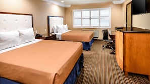 A hotel room with two beds, a desk, a chair, a television, and a window with blinds.