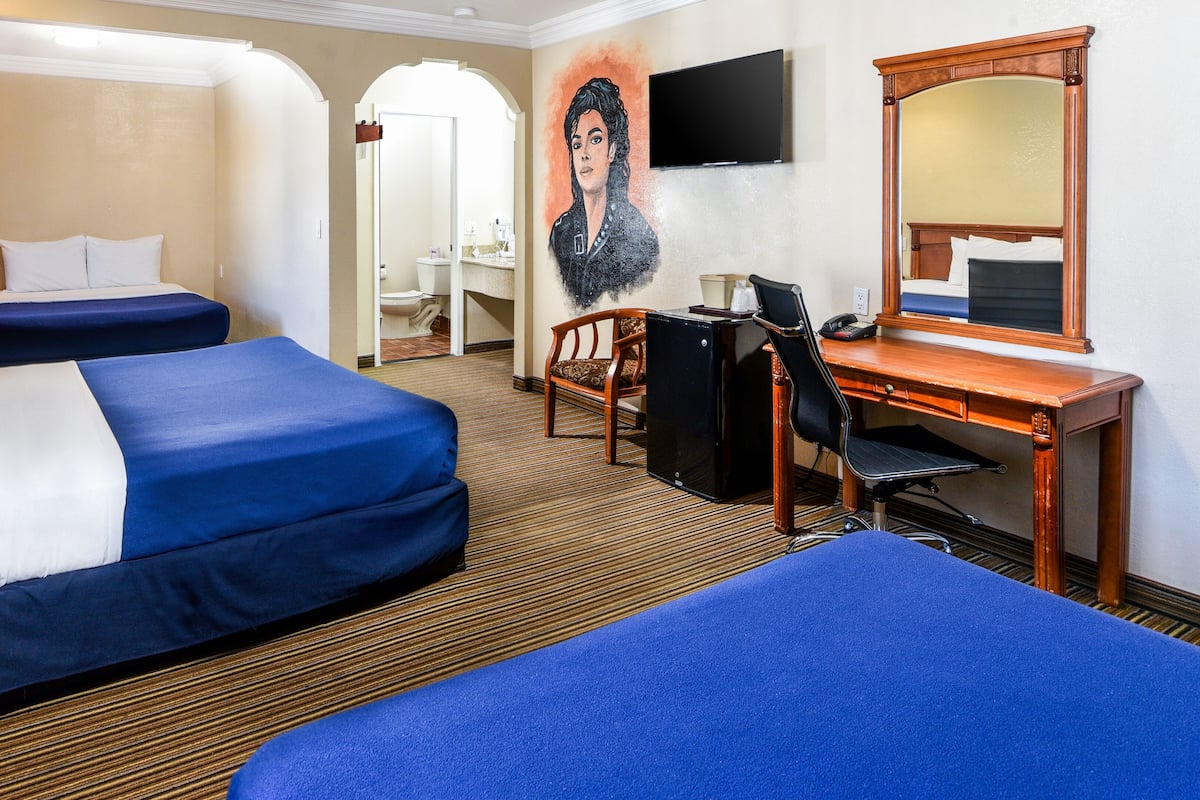 Habitación de hotel con dos camas, un escritorio, una silla, un televisor y un espejo.