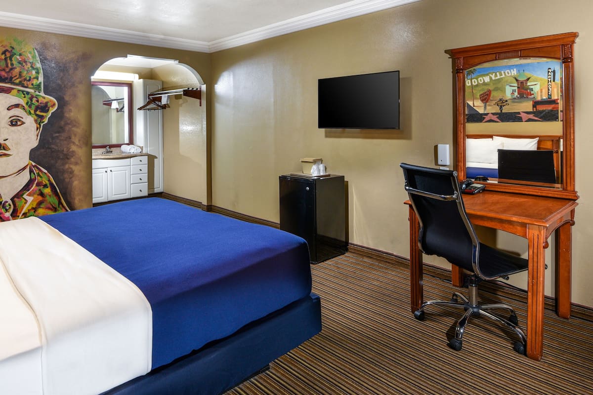 Habitación de hotel con cama, escritorio, silla, televisor y un cuadro en la pared.