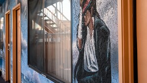 A corridor with a mural of a person in a white shirt and red headscarf, a window, and wooden doors. - Hollywood Inn Express North (Los Angeles)
