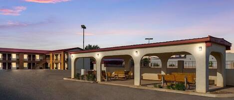 A motel with a covered outdoor seating area and a parking lot.