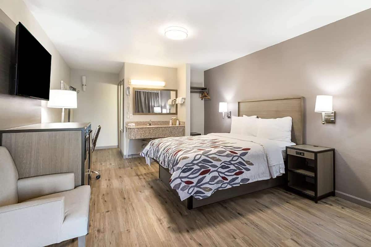 A hotel room with a bed, bedside table, chair, and a TV mounted on the wall.