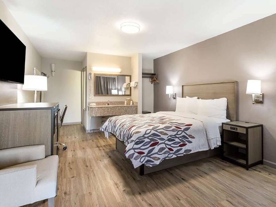 A hotel room with a bed, bedside table, chair, and a TV mounted on the wall.