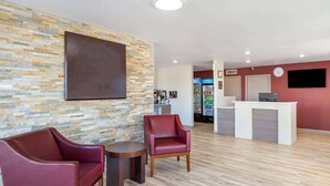 A hotel lobby with a stone wall, two red leather chairs, a reception desk, and a coffee machine. - Baymont by Wyndham Socorro (Socorro)
