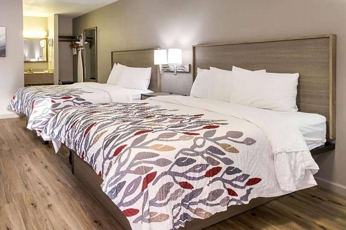A hotel room with a large bed, a wooden floor, a bathroom with a mirror, and a nightstand with a lamp.