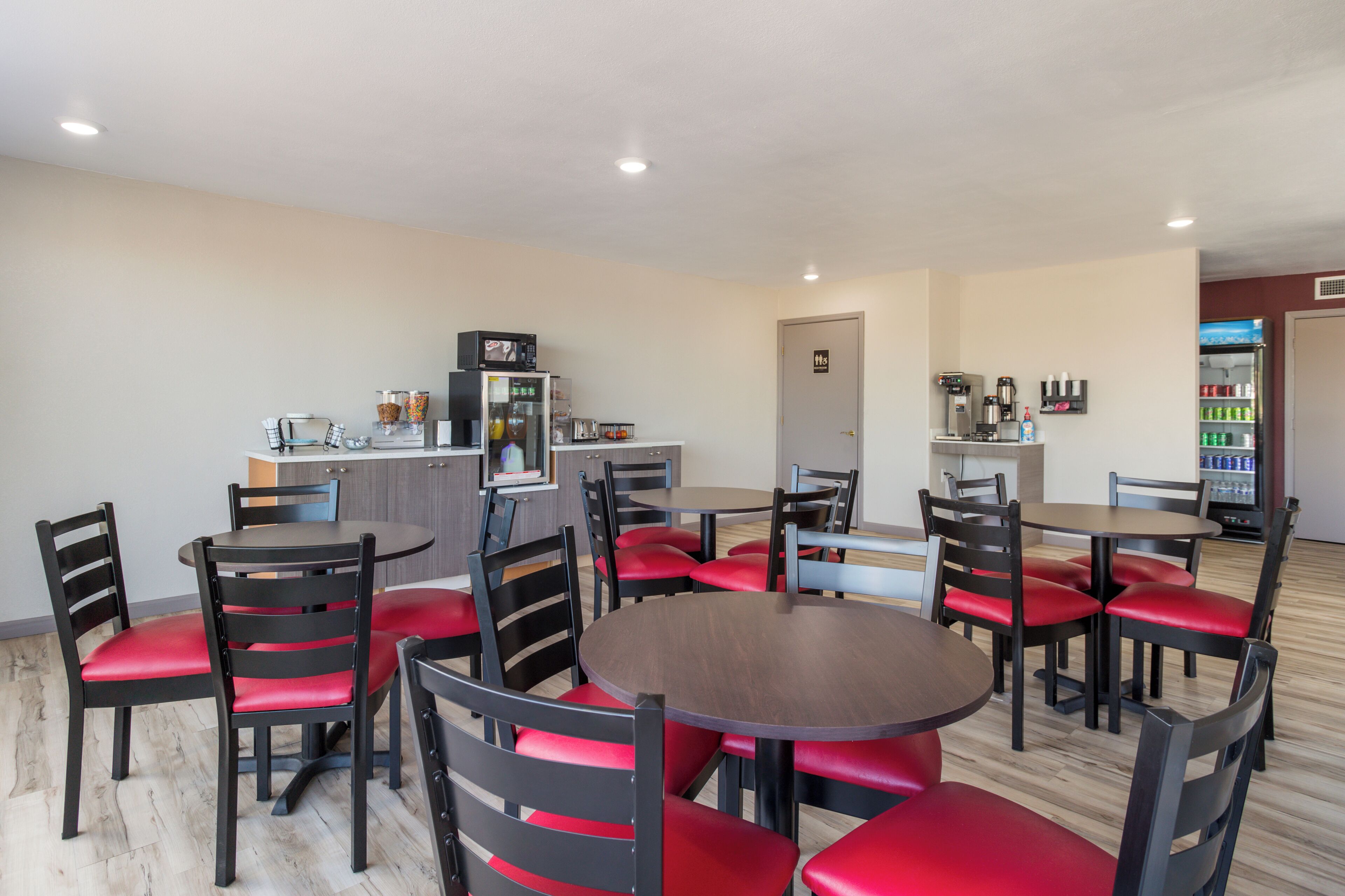 A dining area with round tables and chairs, a kitchen area with appliances, and a refrigerator stocked with beverages.