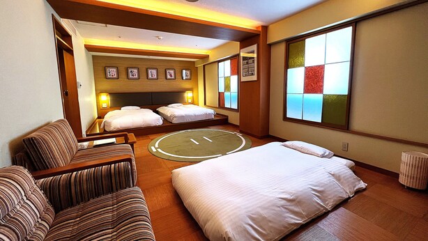 Habitación de hotel con cama, dos sofás, alfombra redonda y un gran ventanal con vistas.