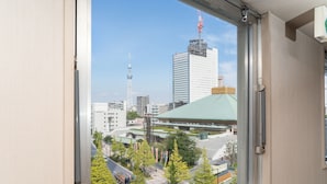 Vista desde una ventana que da a un paisaje urbano con edificios altos, incluyendo una torre destacada y un rascacielos moderno.