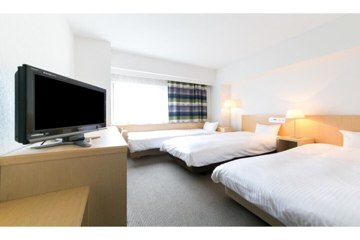 A hotel room with two beds, a desk with a flat-screen TV, bedside lamps, and a window with curtains.