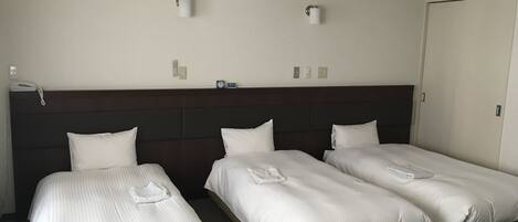 Une chambre d’hôtel avec trois lits simples, une tête de lit sombre, un mur blanc et une porte.