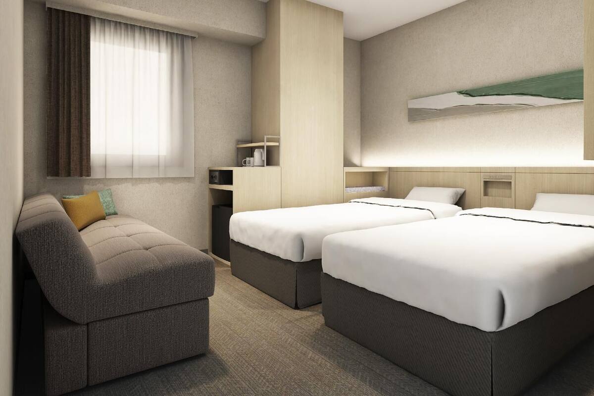 Een hotelkamer met twee bedden, een bank, een bureau en een televisie aan de muur.