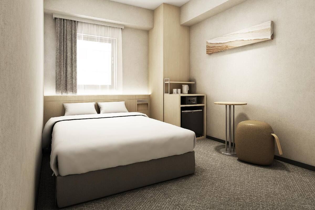 Een hotelkamer met een bed, een kleine tafel, een stoel, een kledingkast en een raam met gordijnen.