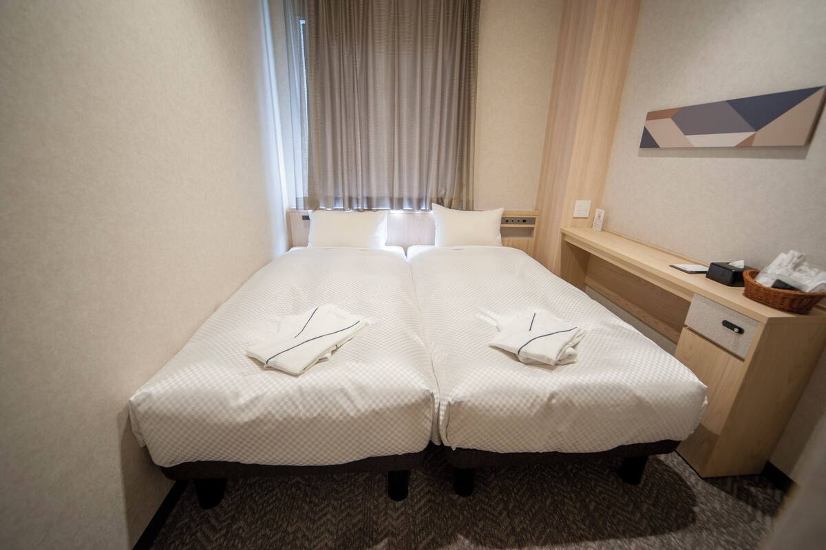 Een hotelkamer met twee enkele bedden, een bureau met een stoel, een klein tafeltje en een televisie aan de muur.