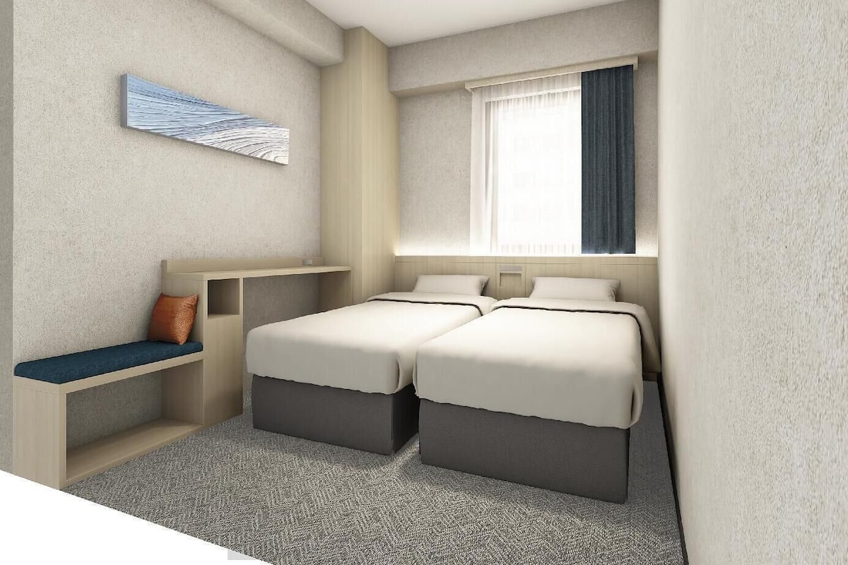 Een hotelkamer met twee bedden, een bureau, een stoel, een raam met gordijnen en een kunstwerk aan de muur.