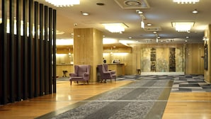 A lobby with a reception desk, two armchairs, a patterned carpet, and a wooden column. - Karasuma Kyoto Hotel (Kyoto)