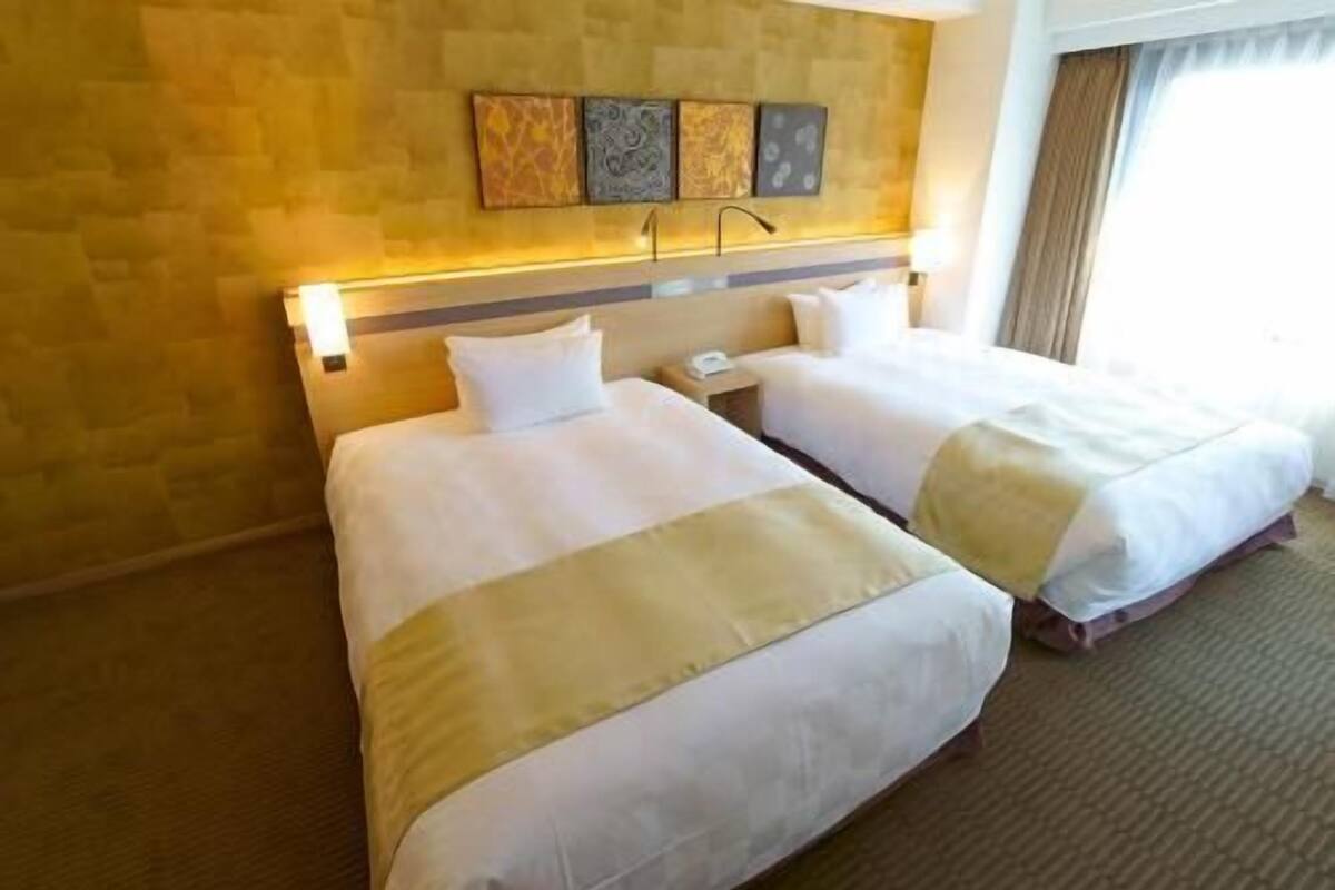 A hotel room with two beds, a headboard with wall art, a nightstand, and a window with curtains.