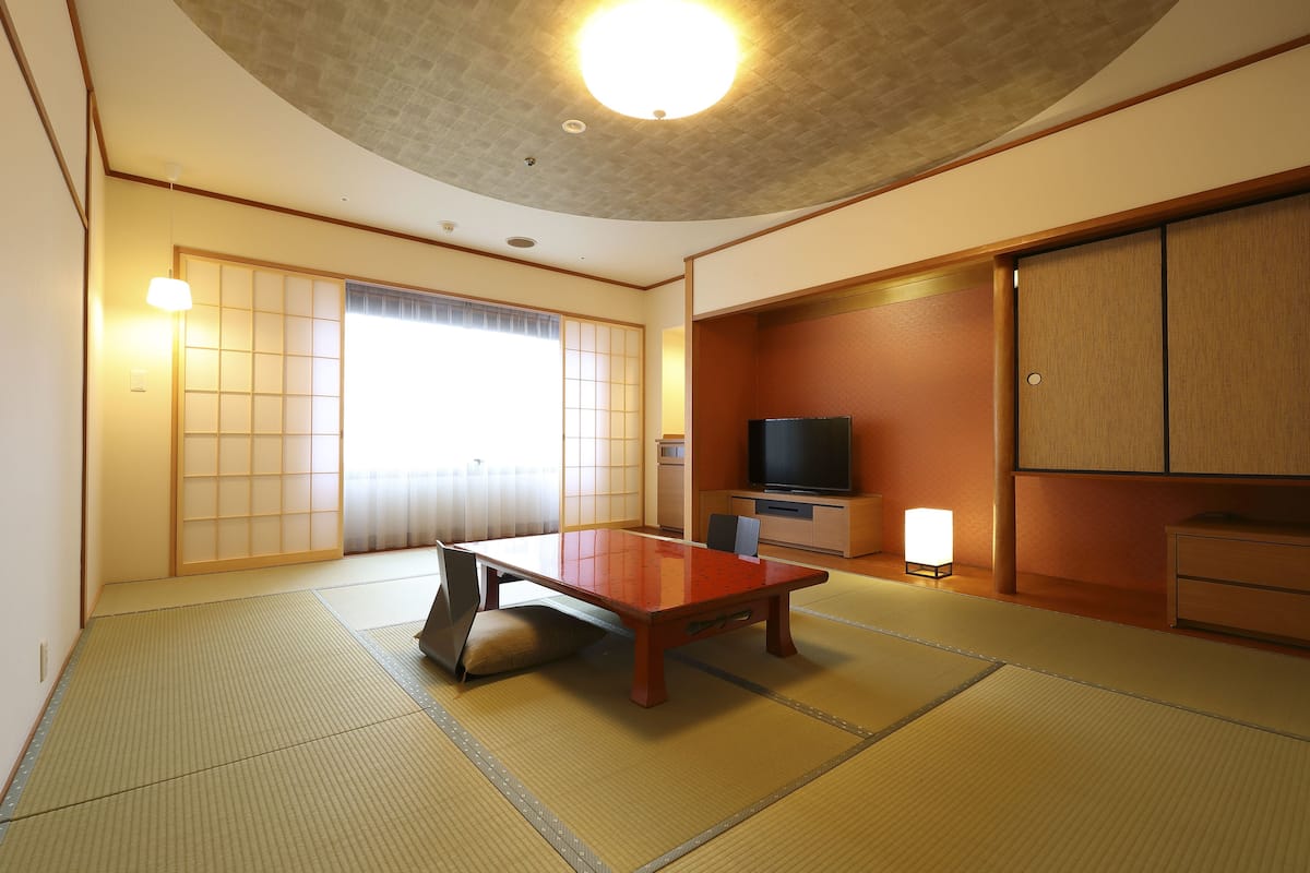 Una habitación japonesa tradicional con suelo de tatami, una mesa baja, puertas correderas y un televisor.