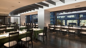 A modern dining area with multiple tables and chairs, large windows, and a contemporary ceiling design. - Karasuma Kyoto Hotel (Kyoto)