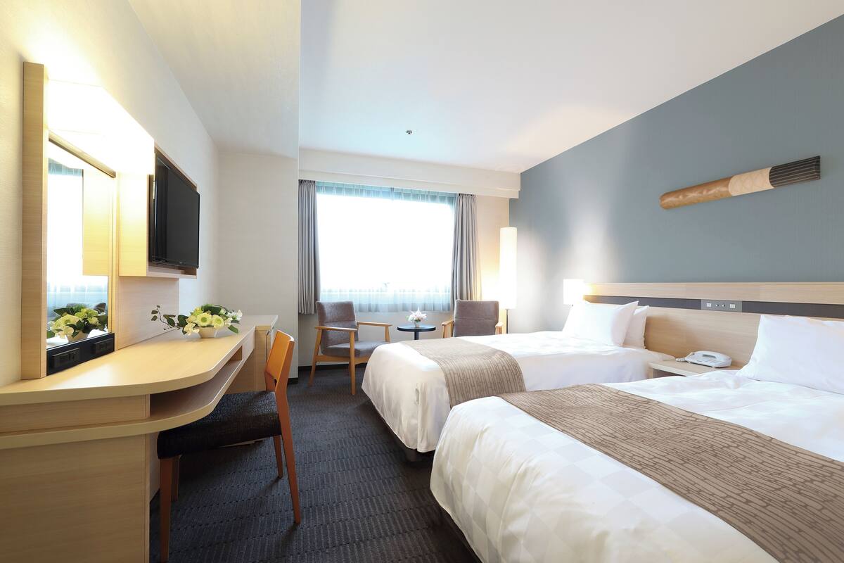 Habitación de hotel con dos camas, un escritorio, una silla, una mesita y un televisor.