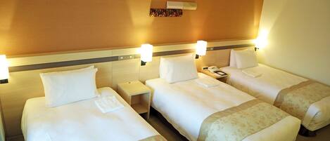 A hotel room with three single beds, each with a nightstand and a lamp.