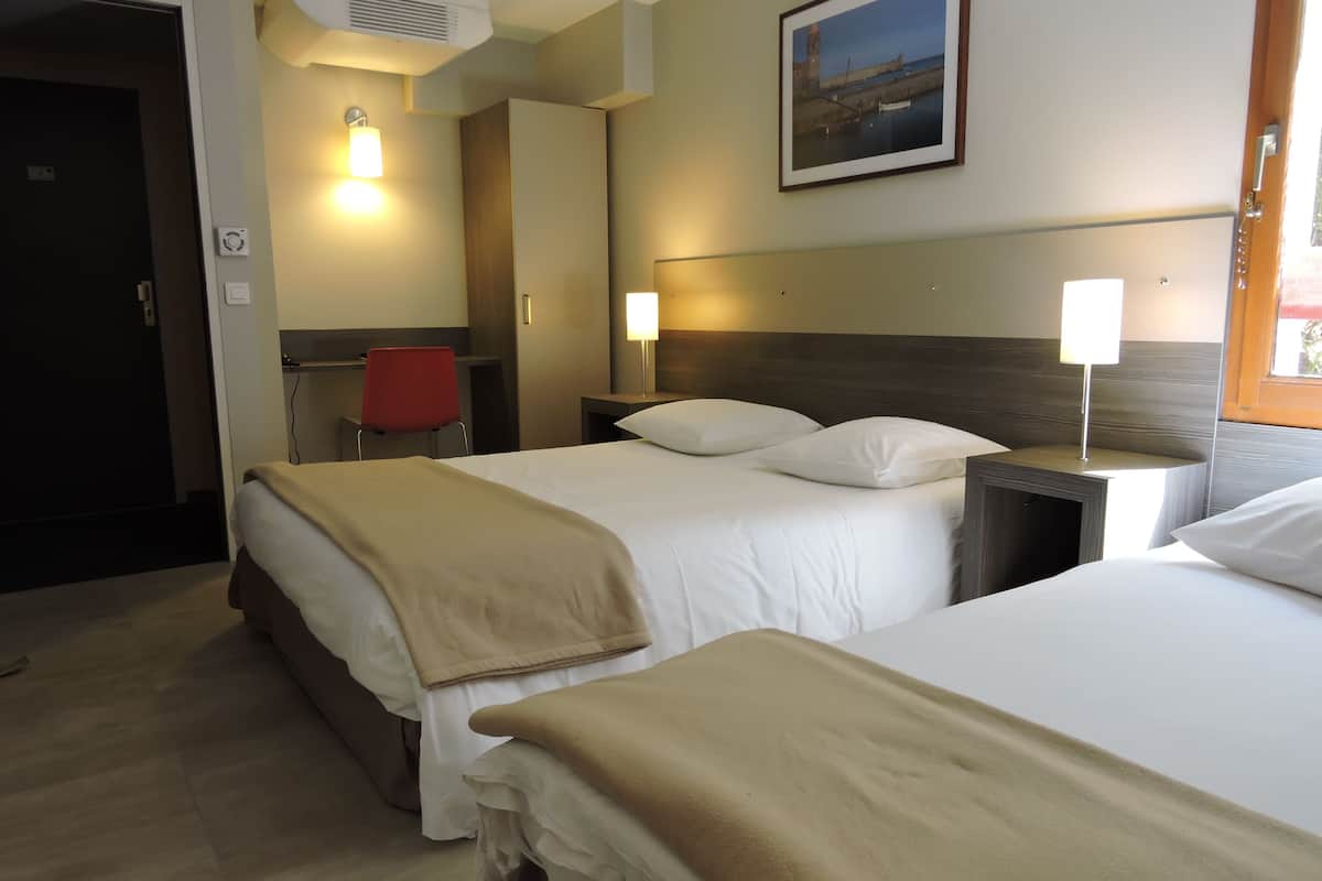 Une chambre d’hôtel avec deux lits, un bureau, une chaise et un tableau au mur.