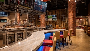A bar area with a curved counter, multiple seating options, and a television screen displaying sports. - Harrah's Kansas City Hotel & Casino - A Caesars Rewards Destination (North Kansas City)