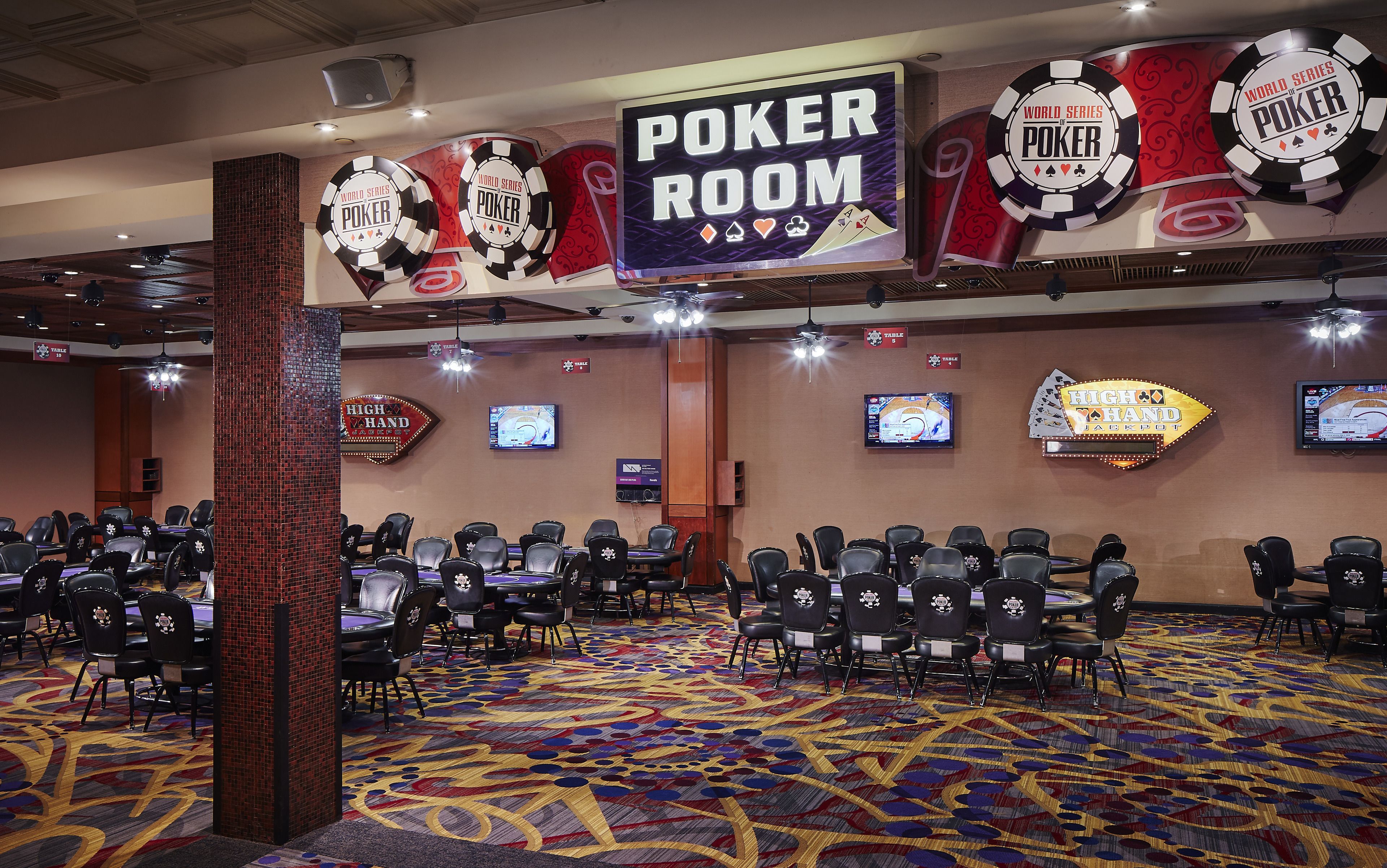 A large room with multiple poker tables and chairs, decorated with poker-themed banners and signs.