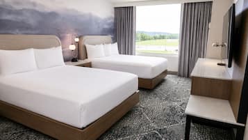 A hotel room with two beds, a desk, a TV, and a large window with a view of the outdoors.