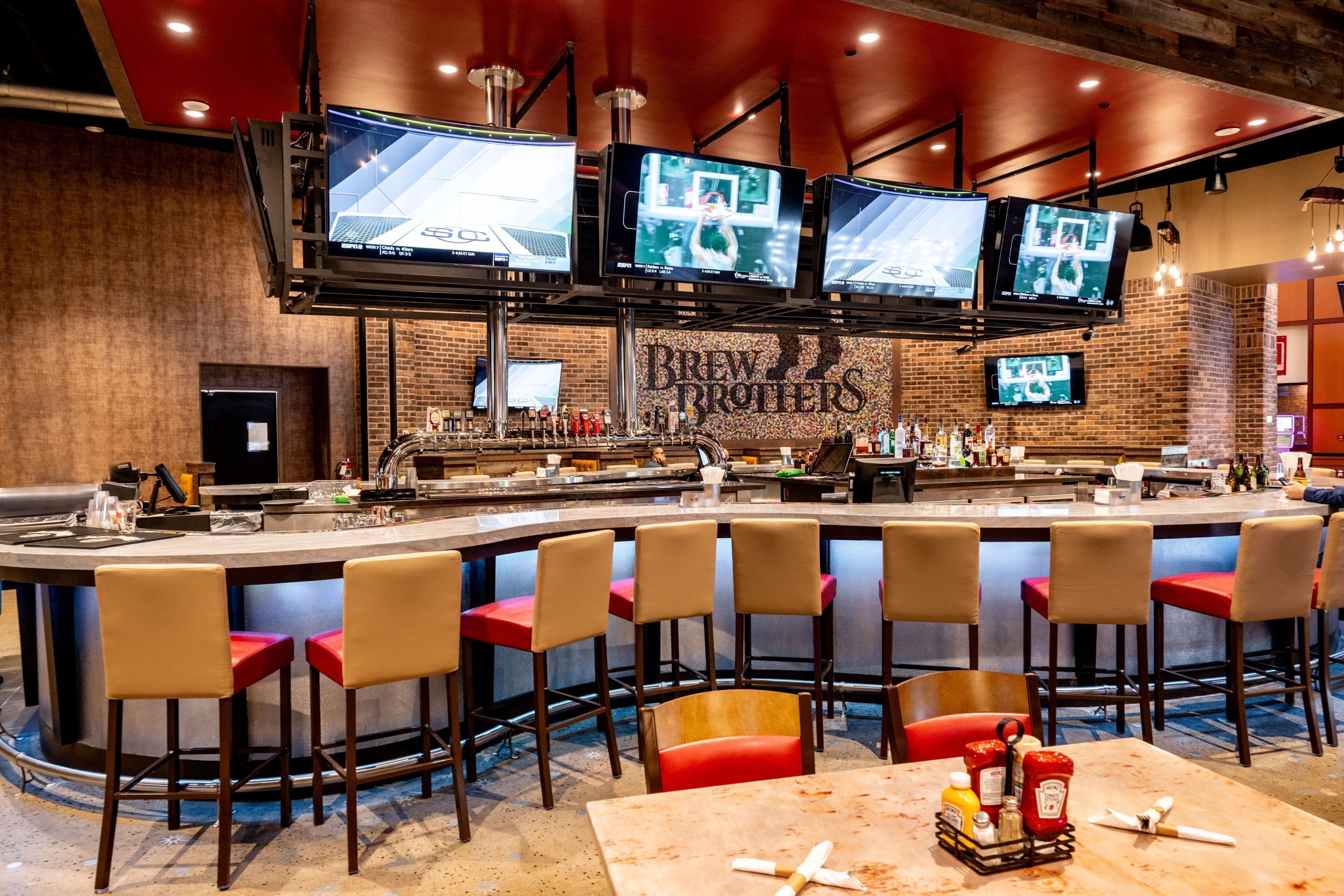 A bar area with multiple screens, a counter, and bar stools.