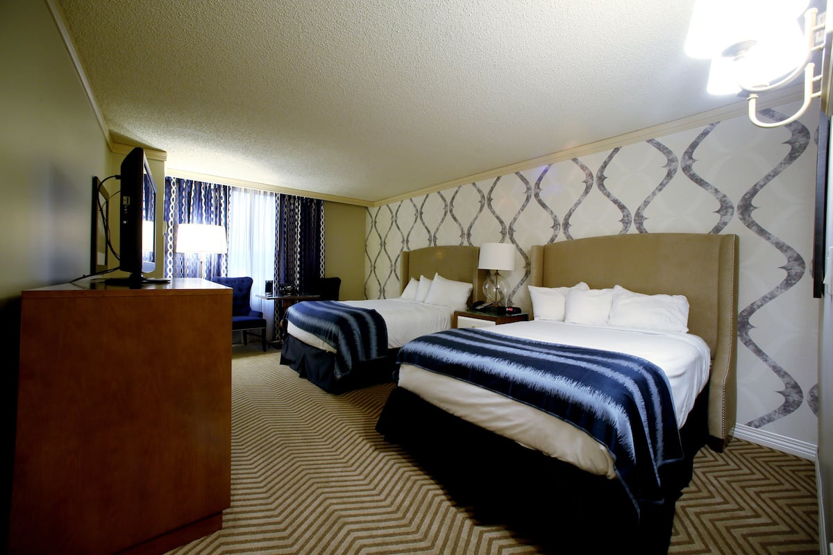 A hotel room with two beds, a desk, and a TV.