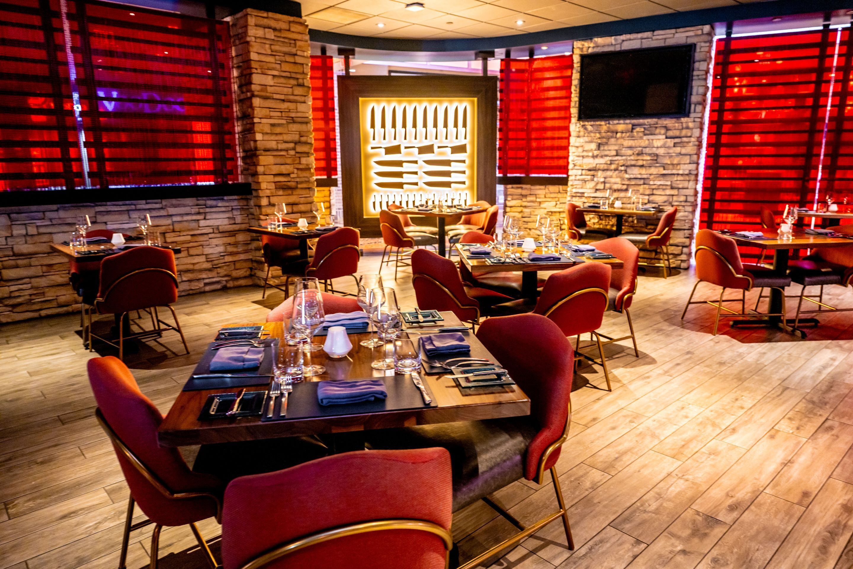 Un restaurante con suelo de madera, sillas tapizadas en rojo y mesas dispuestas para comer.