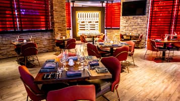 Un restaurante con suelo de madera, sillas tapizadas en rojo y mesas dispuestas para comer.
