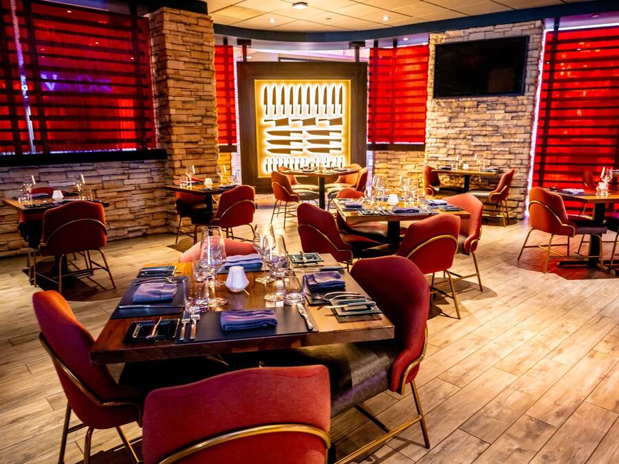 Un restaurante con suelo de madera, sillas tapizadas en rojo y mesas dispuestas para comer.