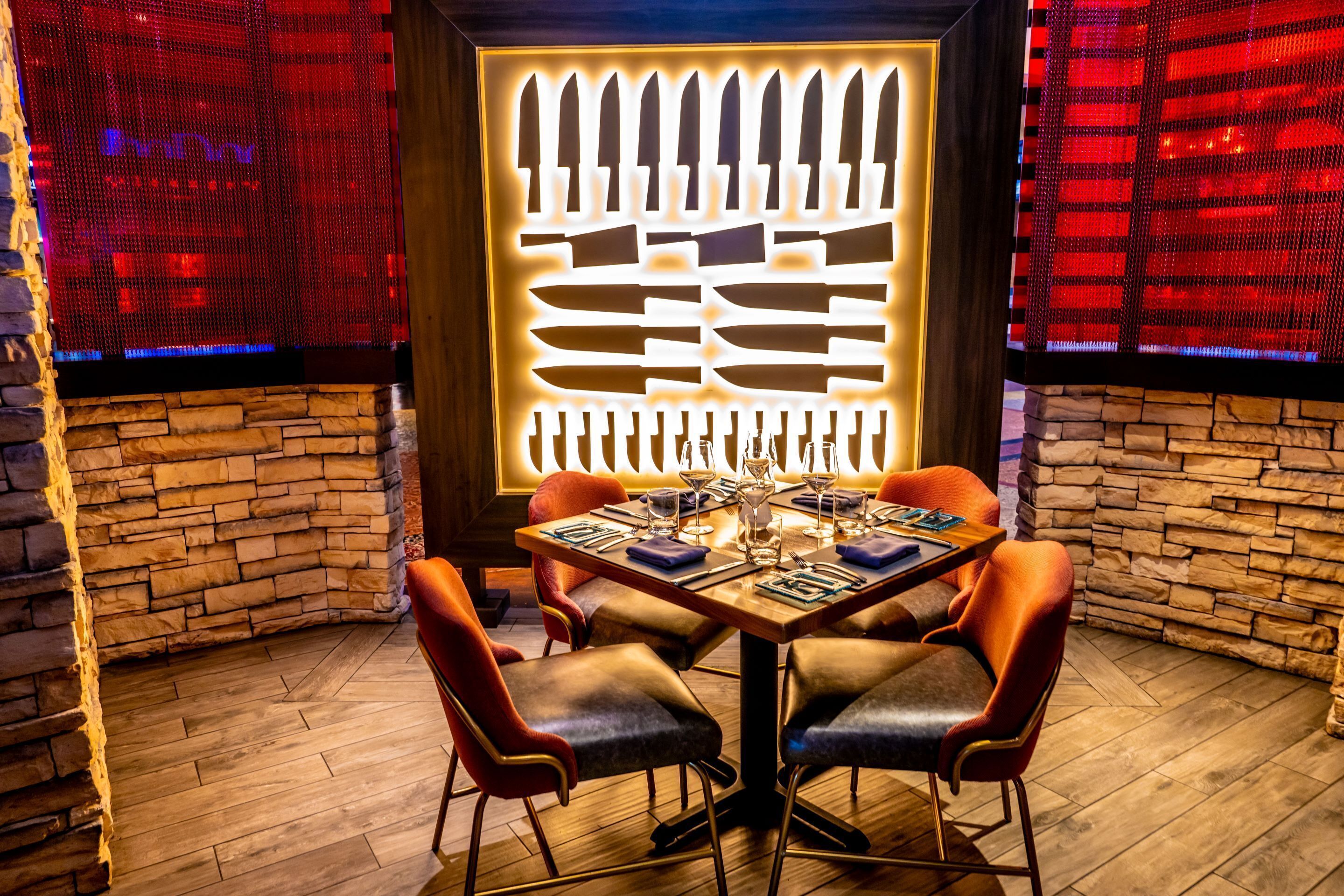 Un comedor con pared de piedra, un panel decorativo con formas recortadas y una mesa para cuatro personas con sillas.