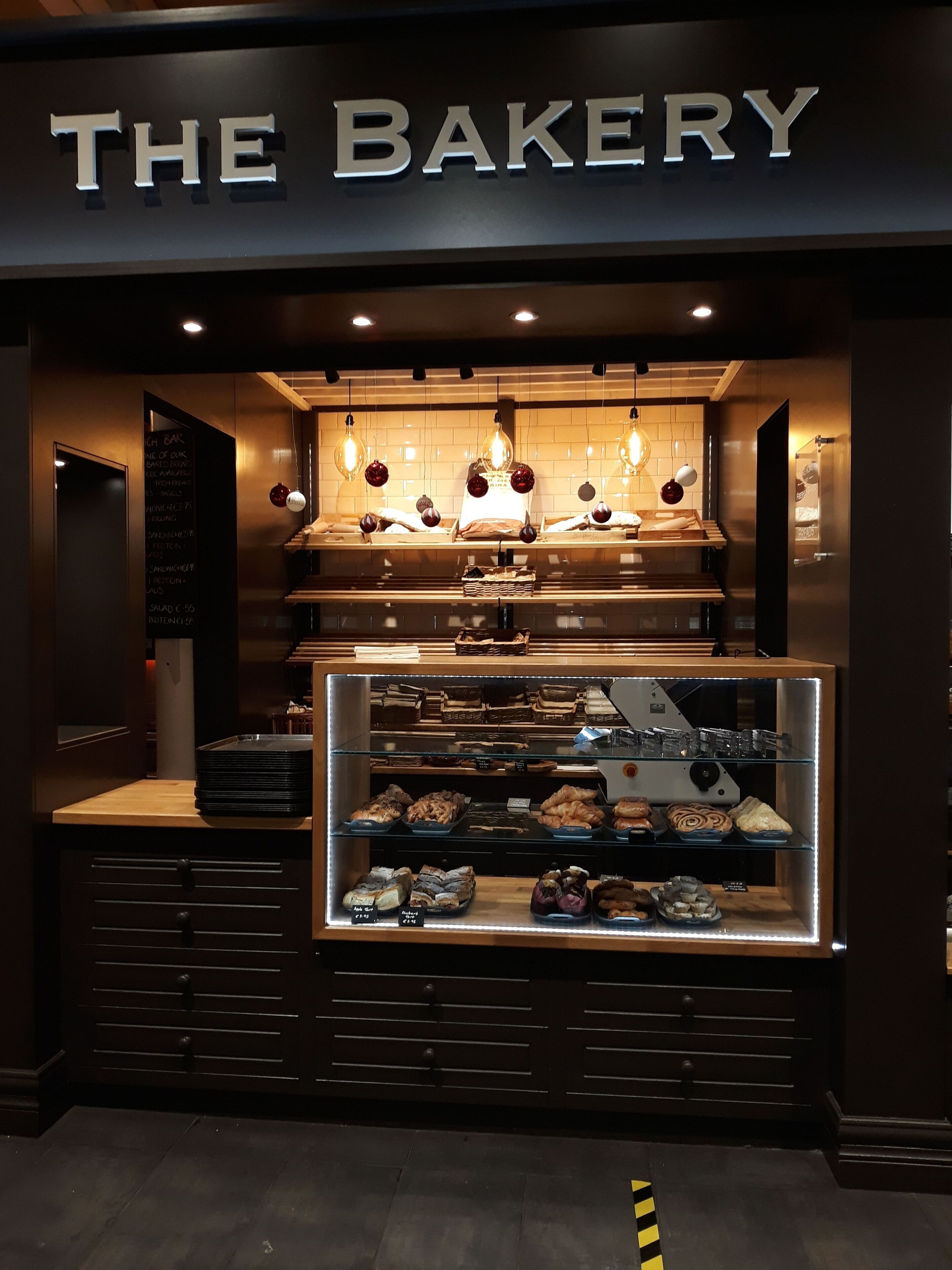 A bakery with a sign reading "THE BAKERY" above a display case filled with pastries.