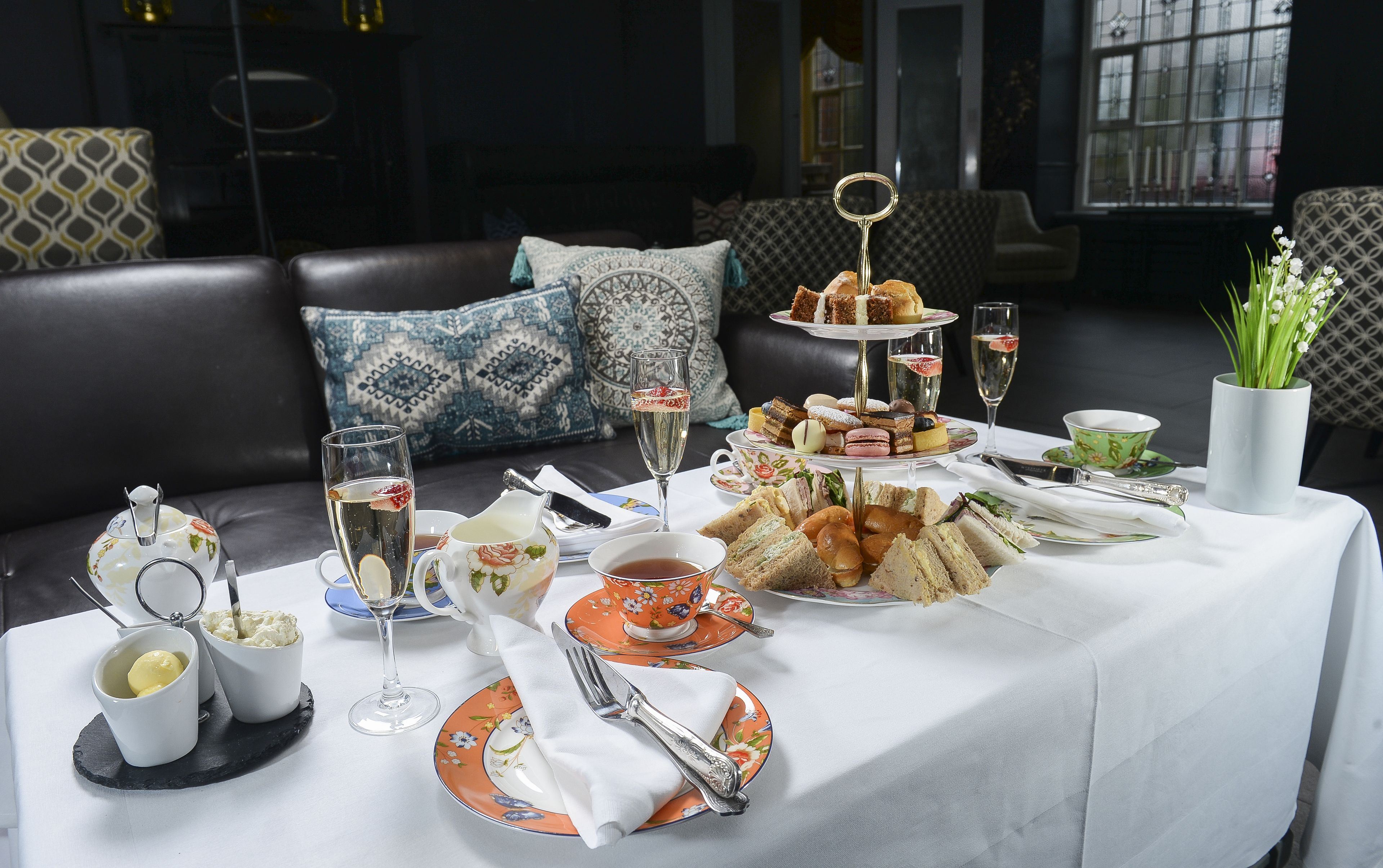 A table set for a tea service with various pastries and sandwiches, accompanied by tea cups and glasses.