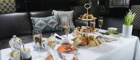 A table set for a tea service with various pastries and sandwiches, accompanied by tea cups and glasses.