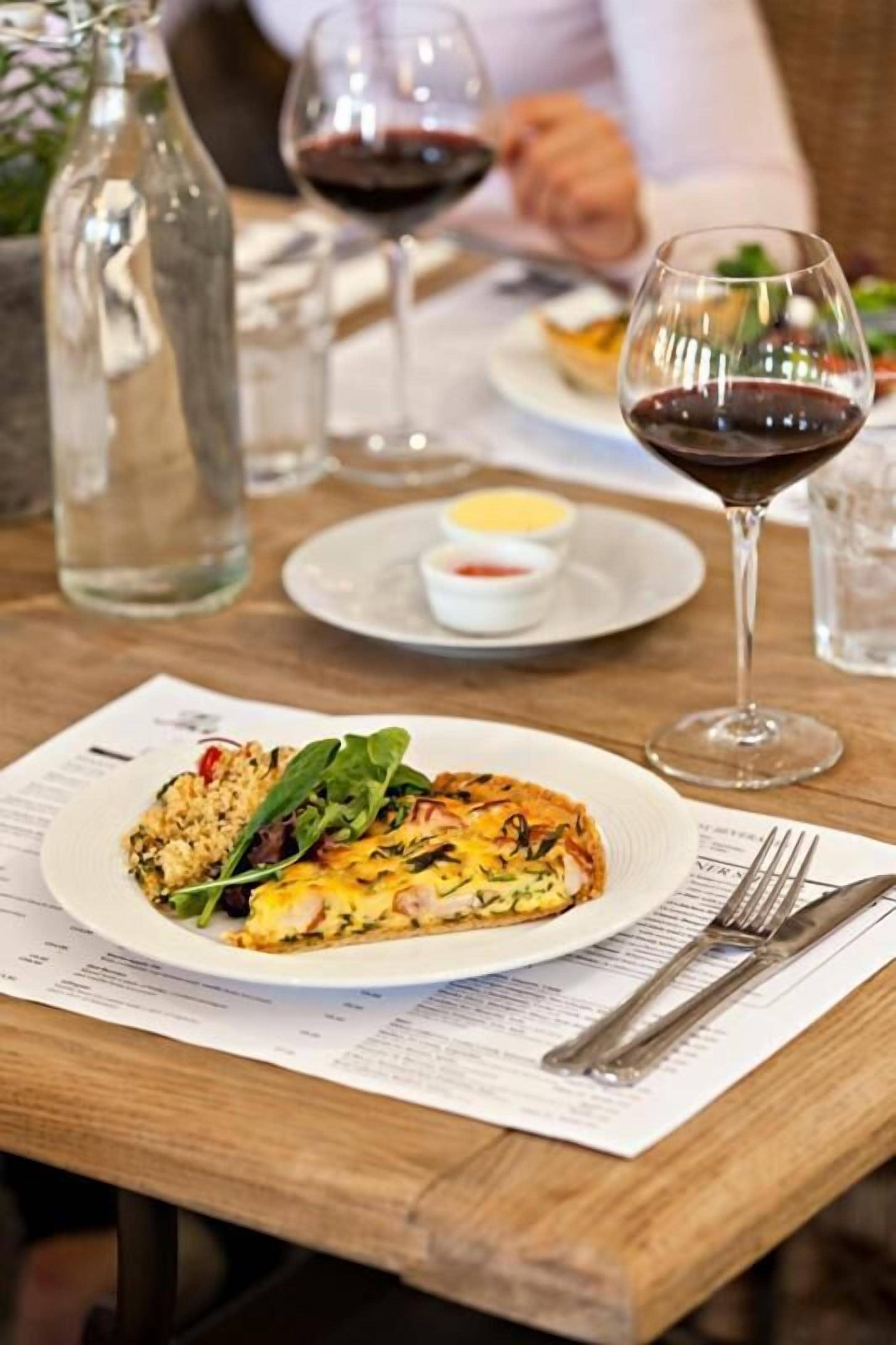 A dining table with a plate of food, a wine glass, and a menu.