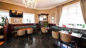 A lobby with a chandelier, a television, a large mirror, and seating areas.