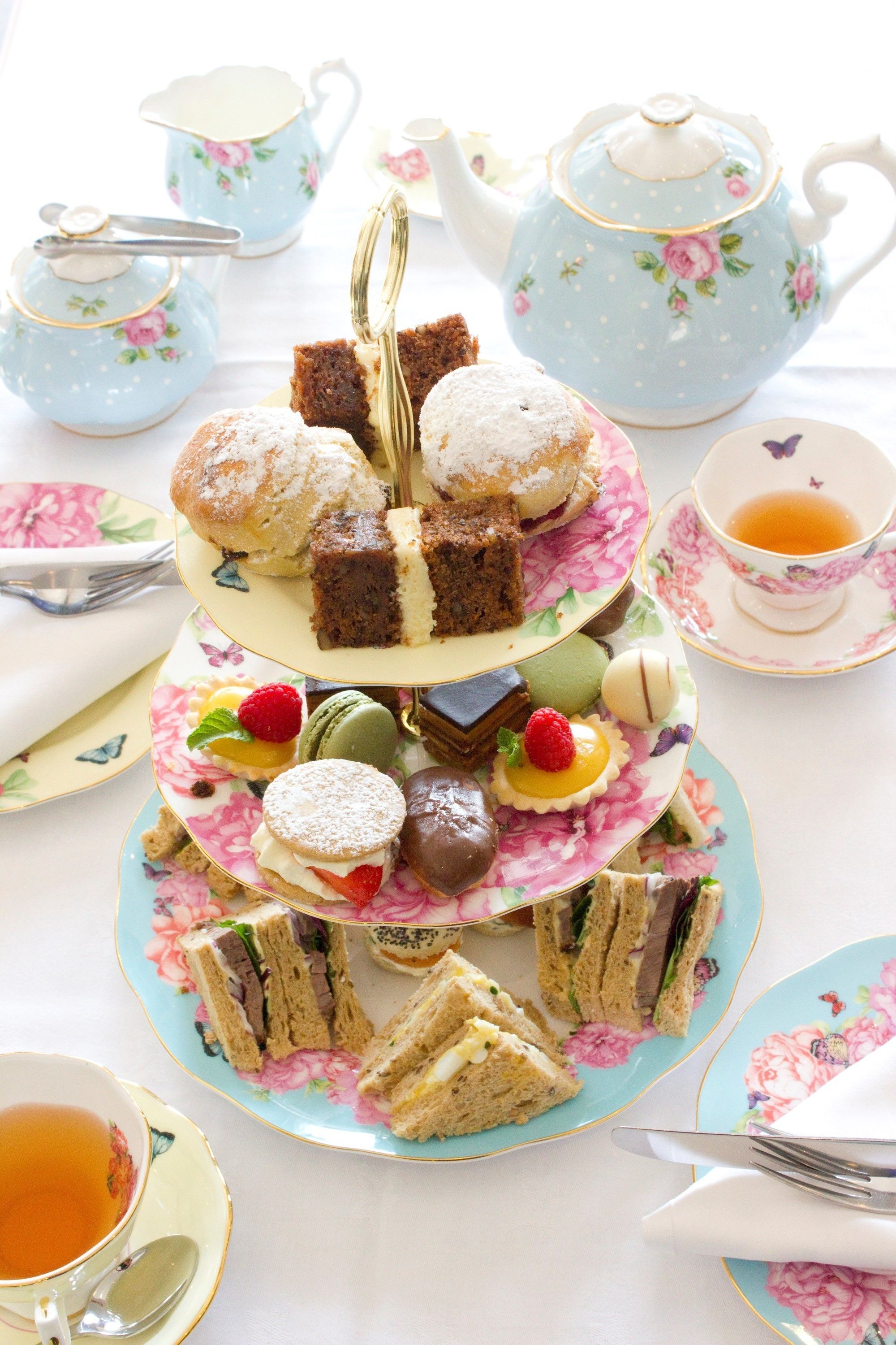 A tiered dessert stand with various pastries and sandwiches, accompanied by tea sets and a teapot.